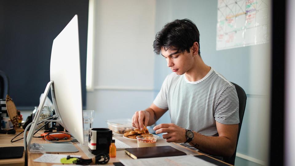 A young man eats lunch at his desk in the office.