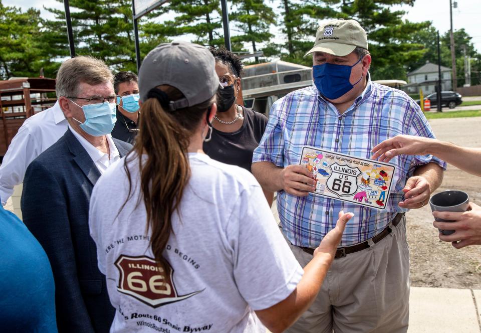 Illinois Gov. JB Pritzker receives a Route 66 license plate and a hat from Casey Wichmann, Route 66 Scenic Byway Executive Director after the ribbon cutting ceremony for the Route 66 Experience during the 2021 Illinois State Fair at the Illinois State Fairgrounds in Springfield, Ill., Friday, August 13, 2021. The Route 66 Experience is a multiyear project focusing on the iconic road that will culminate in the  centennial celebration in 2026. [Justin L. Fowler/The State Journal-Register] 