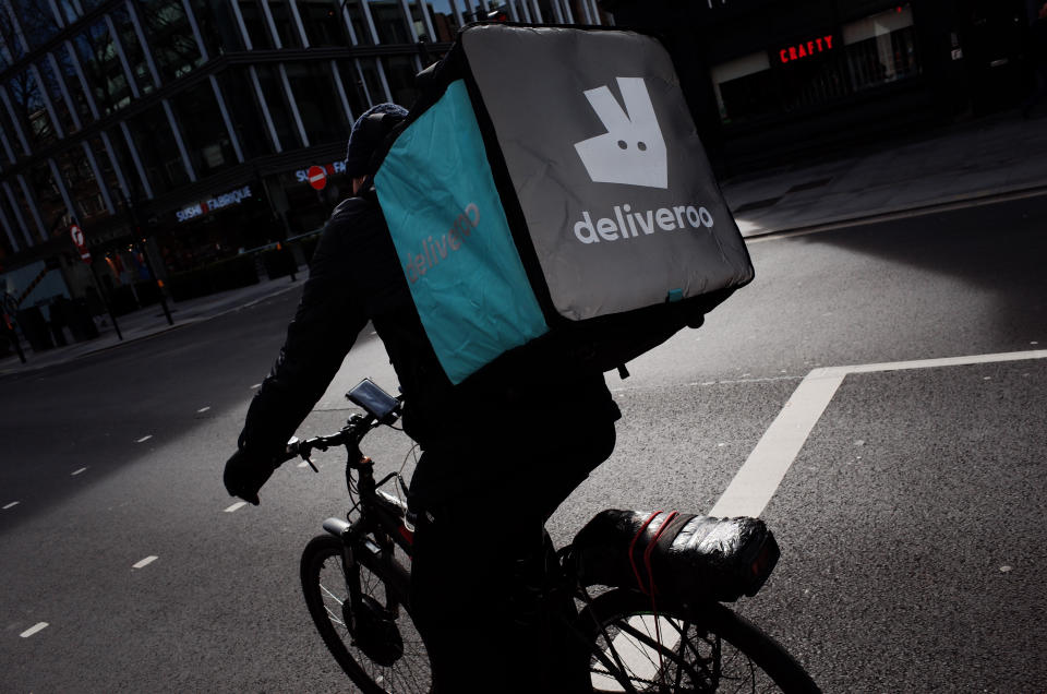 A Deliveroo courier cyclist waits at traffic lights on a near-deserted Tottenham Court Road in London, England, on March 21, 2020. Much of central London was virtually empty today, a day after British Prime Minister Boris Johnson ordered the closure of all pubs, bars, cafes and restaurants around the country. The move represents a toughening of measures to enforce the 'social distancing' that is being urged on citizens to reduce the growth of covid-19 coronavirus infections. Nightclubs, theatres, cinemas, gyms and leisure centres were also ordered closed. Some shops in the centre of capital remained open today, albeit mostly deserted of customers; many retailers however have temporarily closed their doors until the crisis abates. (Photo by David Cliff/NurPhoto via Getty Images)