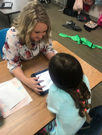 Former Oklahoma teacher Chelsea Price, 34, helps a 2nd grade student with an assignment on an iPad in her classroom in Grapevine, Texas, U.S., April 4, 2018. Courtesy Chelsea Price/Handout via REUTERS