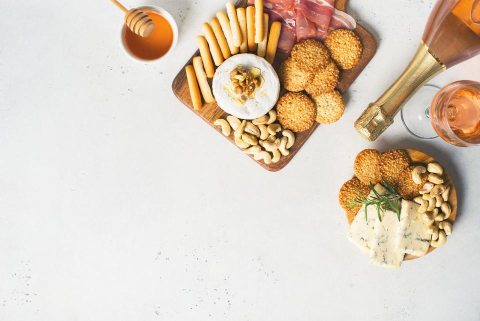 wooden board with cheese, ham, bread stick, nut cashew, walnut and honey on camembert with glasses of wine on white background