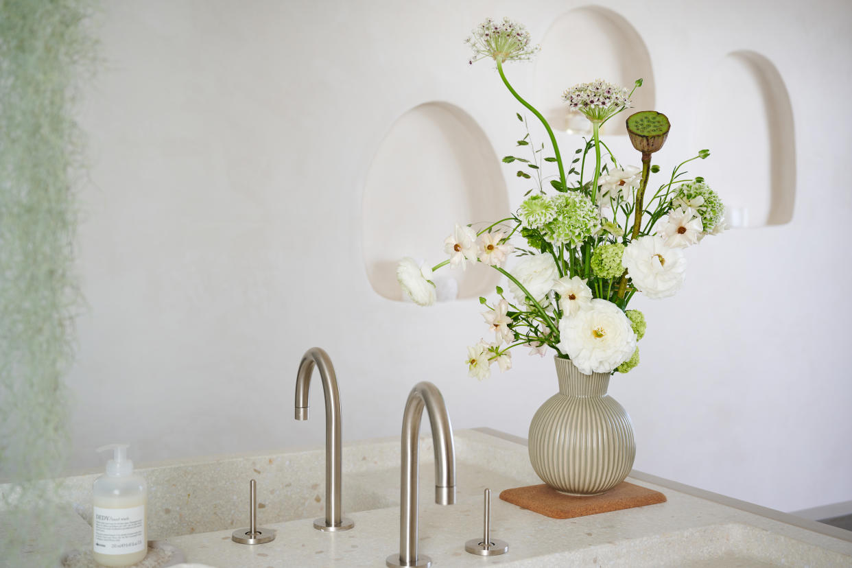  A glass vase filled with white flowers and foliage next to a kitchen sink. 