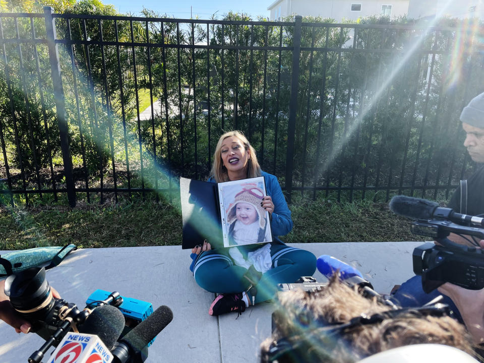 Brazilian American Vanessa Viana holds a picture of her son when he was a baby outside the house where Brazil's former President Jair Bolsonaro is staying in Florida. (Suzanne Gamboa / NBC News)