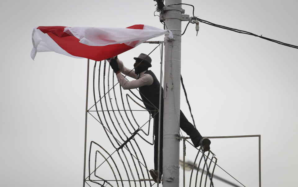 A man in a mask hangs an old Belarusian flag on a light pole during an opposition rally to protest the official presidential election results in Minsk, Belarus, Sunday, Sept. 27, 2020. Hundreds of thousands of Belarusians have been protesting daily since the Aug. 9 presidential election. (AP Photo/TUT.by)