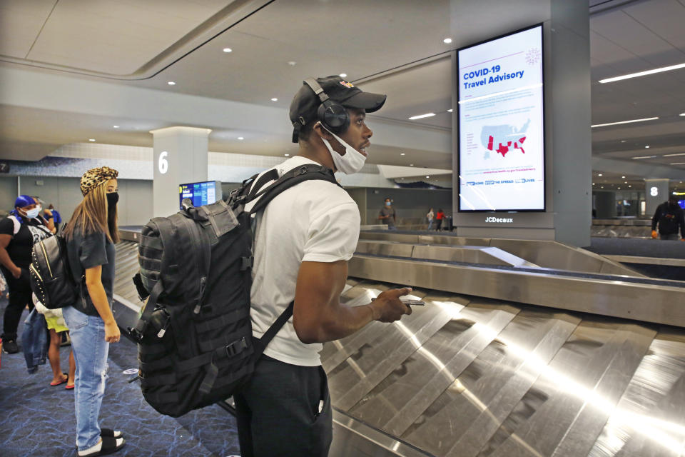 Arriving passengers await their bags in the baggage claim area at LaGuardia Airport's Terminal B baggage claim area, Thursday, June 25, 2020, in New York. New York, Connecticut and New Jersey are asking visitors from states with high coronavirus infection rates to quarantine for 14 days. (AP Photo/Kathy Willens)
