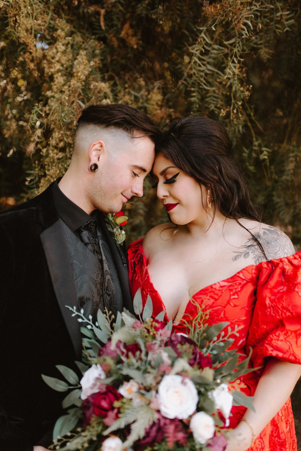 A man in a black suit and a woman in a red dress press their heads together.