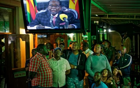 Zimbabweans watch a televised address to the nation by President Robert Mugabe at a bar in downtown Harare, - Credit: AP