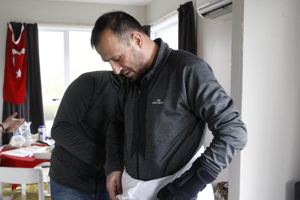 In this July 31, 2019, photo, Temel Atacocugu, who was shot nine times during the Christchurch mosque attacks, tries on the clothes he will wear during the Hajj pilgrimage, in Christchurch, New Zealand. He is among 200 survivors and relatives from the Christchurch mosque shootings who are traveling to Saudi Arabia as guests of King Salman for the Hajj pilgrimage, a trip many hope will help them to heal.(AP Photo/Nick Perry)
