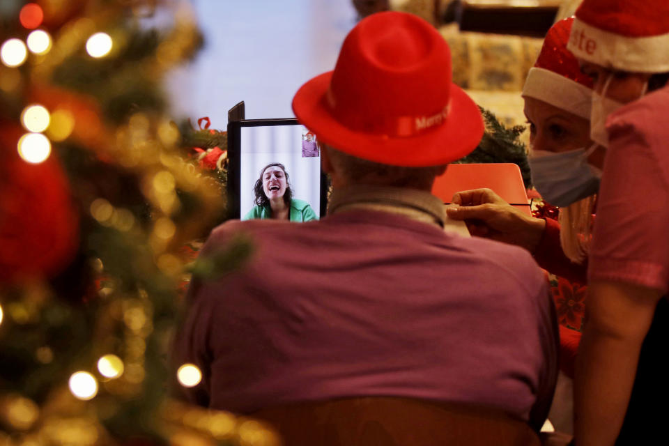 Luigi Zanini flanked by director Maria Giulia Madaschi, talks via video call with Ilaria Sacco a donor unrelated to him who bought and sent her a Christmas present through an organization dubbed "Santa's Grandchildren", at the Martino Zanchi nursing home in Alzano Lombardo, one of the area that most suffered the first wave of COVID-19, in northern Italy, Saturday, Dec. 19, 2020. (AP Photo/Luca Bruno)