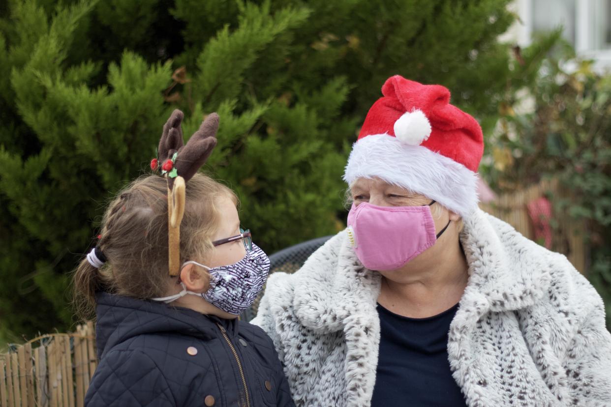 A happy  grandmother with her grandchild outside wearing reindeer antlers and a santa hat and protective face masks.