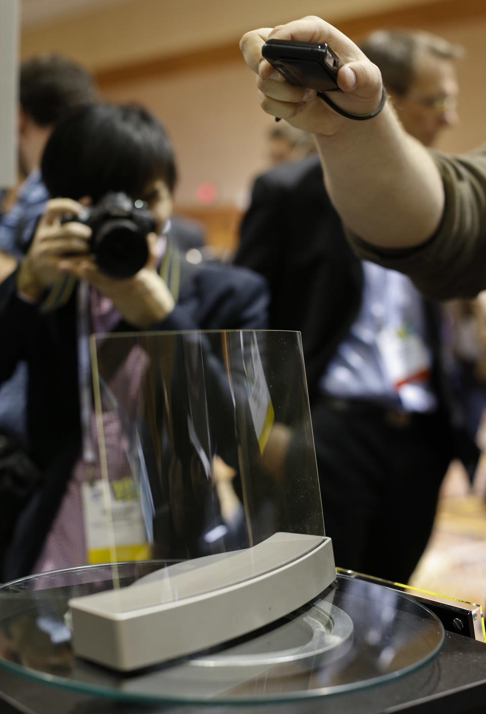Members of the media photograph a glass speaker called Clio during the International Consumer Electronics Show, Sunday, Jan. 5, 2014, in Las Vegas. The speaker, produced by ClearView Audio uses a single piece of curved millimeter-thick acrylic glass that sits on a dock which vibrates it in a finely tuned way so that it can play music. It works with Bluetooth streaming and with a 3.5 millimeter jack. (AP Photo/Julie Jacobson)