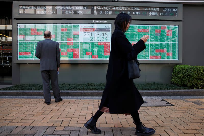 A woman walks past a man examining an electronic board showing Japan's Nikkei average and stock quotations in Tokyo