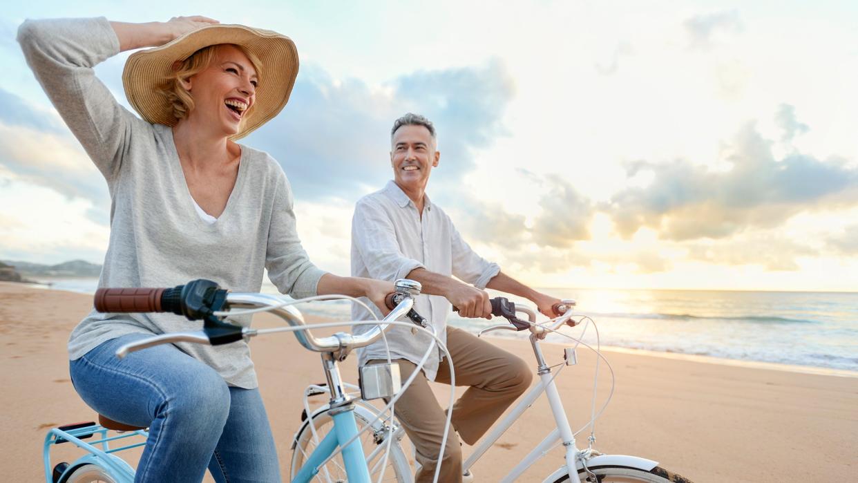 Mature couple cycling on the beach at sunset or sunrise.