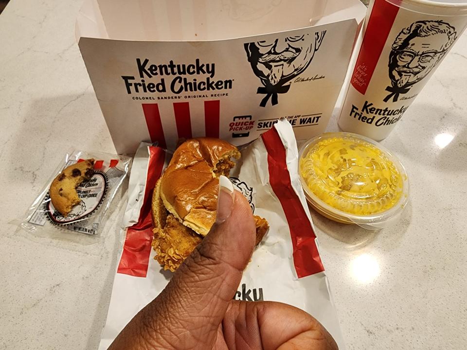 The writer holds a thumbs up in front of KFC meal with cookie, sandwich, and mac and cheese