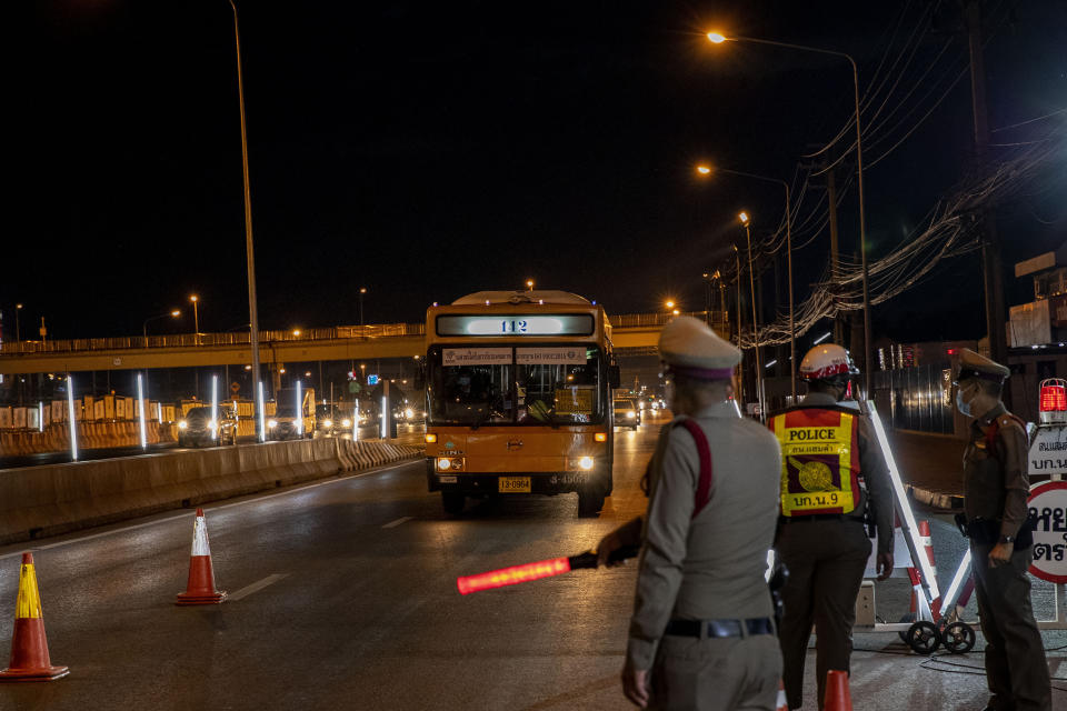 A policeman signals a bus to stop at a check point in the border of Samut Sakhon province and Bangkok in Thailand, Monday, Jan. 4, 2021. For much of 2020, Thailand had the coronavirus under control. After a strict nationwide lockdown in April and May, the number of new local infections dropped to zero, where they remained for the next six months. However, a new outbreak discovered in mid-December threatens to put Thailand back where it was in the toughest days of early 2020. (AP Photo/Gemunu Amarasinghe)