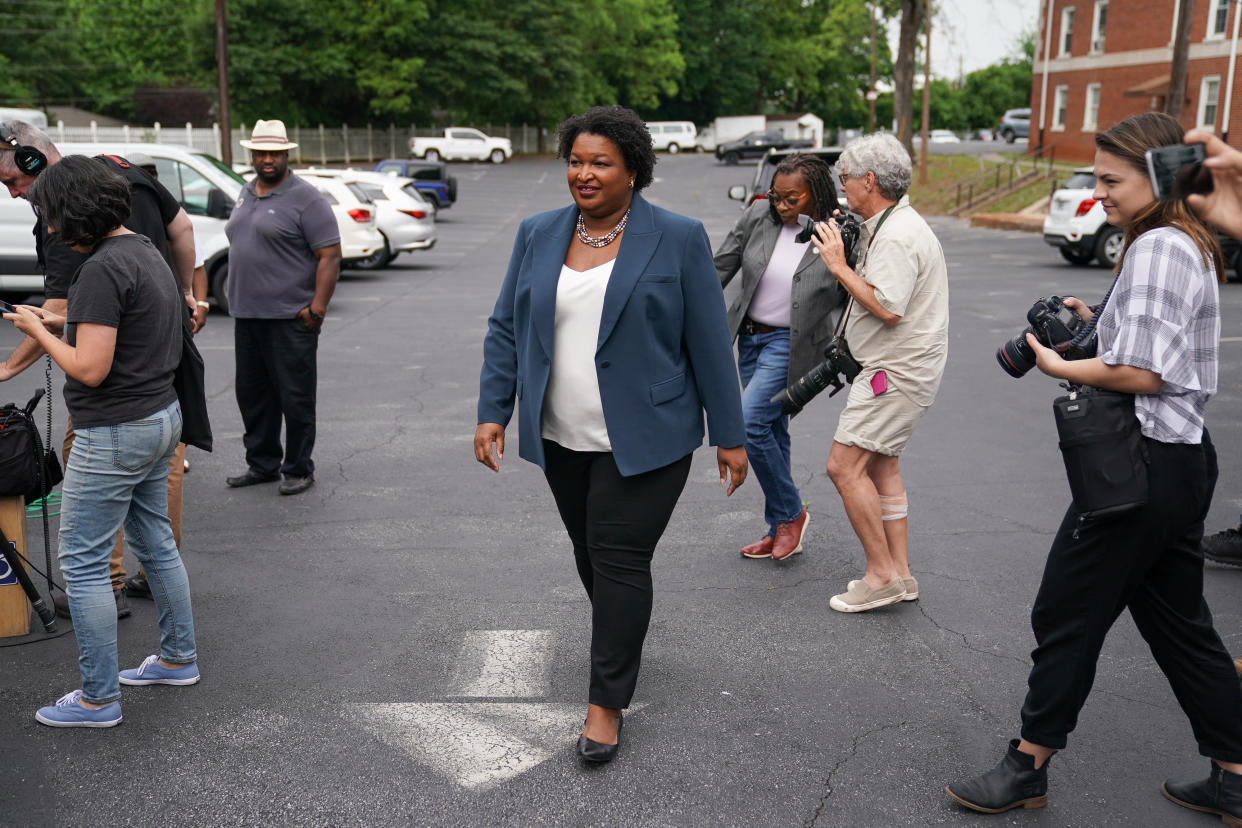 Stacey Abrams, flanked by photographers, walks through a parking lot as she goes to a news conference.