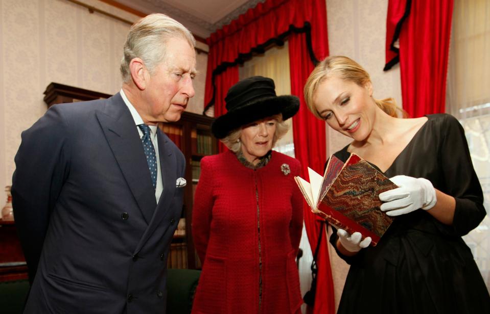 Gillian Anderson shows a first edition of a Charles Dickens book, with the author’s annotations, to Britain’s Prince Charles and his wife Camilla, Duchess of Cornwall, during a tour of the Dickens Museum on February 7, 2012, in London.