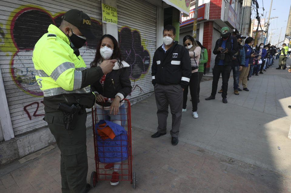 Un oficial de policía observa la identificación de una mujer en una estación de autobuses públicos en Soacha, en las afueras de Bogotá, Colombia, el viernes 27 de marzo de 2020. Las autoridades colombianas han impuesto una cuarentena total y drásticas restricciones de movilización en un esfuerzo por contener la propagación del nuevo coronavirus. (Foto AP/Fernando Vergara)