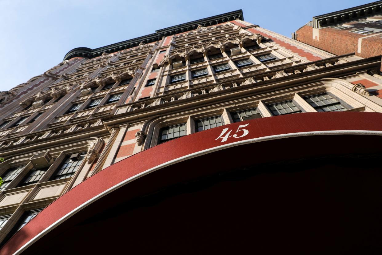 A gothic apartment building facade looms against a blue sky with a red awning in the foreground. The number "45" is on the awning.