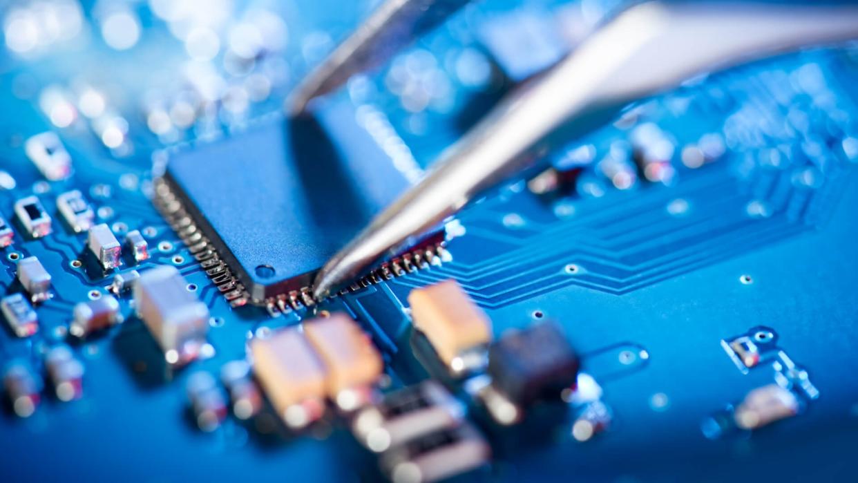 Electronic technician holding tweezers and assemblin a circuit board.