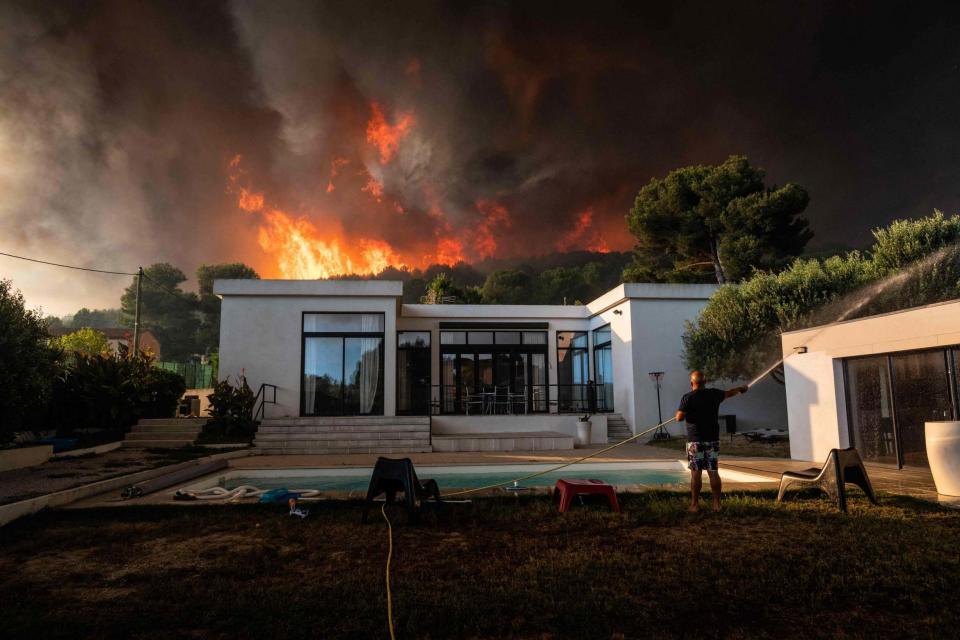 A man uses garden hose to drench his house before being evacuated as a wild fire burns in the background, in La Couronne, near Marseille (AFP via Getty Images)