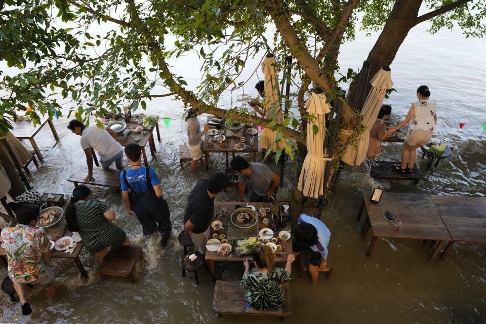 Customers of the riverside Chaopraya Antique Café react to a boat's wake as they enjoy themselves in the extraordinary high water levels in the Chao Phraya River in Nonthaburi, near Bangkok, Thailand, Thursday, Oct. 7, 2021. The flood-hit restaurant has become an unlikely dining hotspot after fun-loving foodies began flocking to its water-logged deck to eat amid the lapping tide. Now, instead of empty chairs and vacant tables, the cafe is as full as ever, offering an experience the canny owner has re-branded as “hot-pot surfing.” (AP Photo/Sakchai Lalit)
