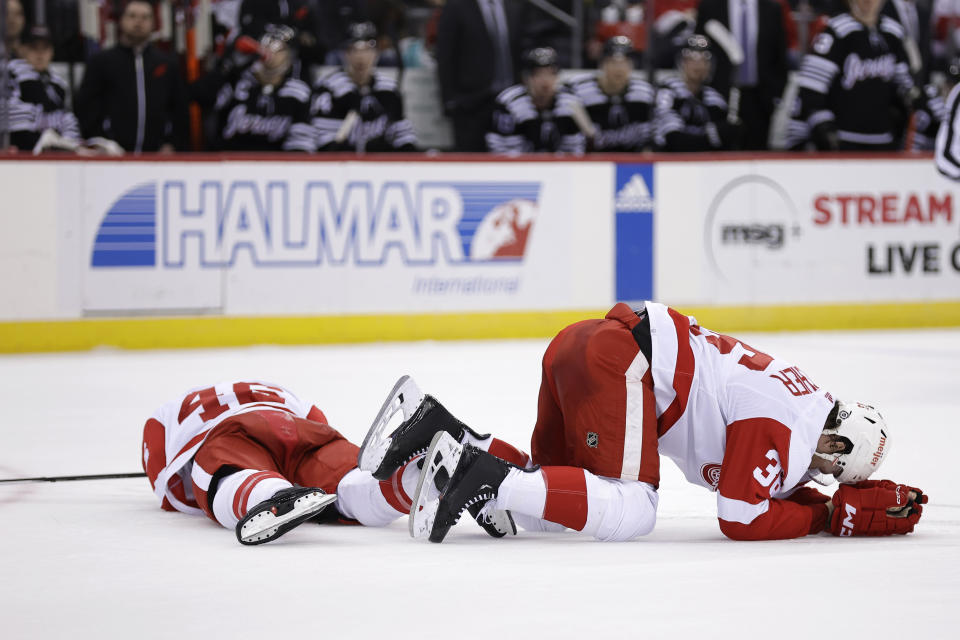Detroit Red Wings right wing Christian Fischer, right, and Jeff Petry lie on the ice after colliding during the second period of the team's NHL hockey game against the New Jersey Devils on Saturday, Dec. 23, 2023, in Newark, N.J. (AP Photo/Adam Hunger)