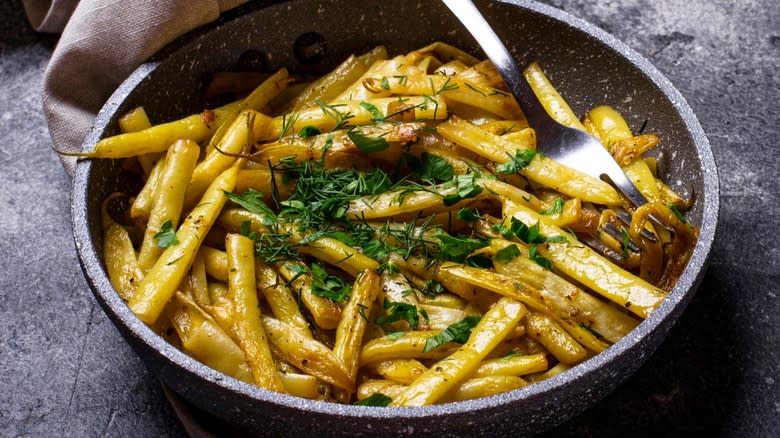 Cooked yellow wax beans in a frying pan with a fork