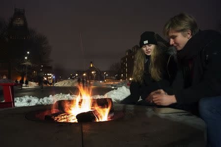 Passers-by sit around a fire pit on cold winter evening outside the Science Center at Harvard University in Cambridge, Massachusetts February 18, 2015. REUTERS/Brian Snyder