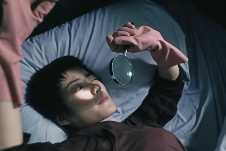 faye wong as faye laying on a bed wearing pink rubber gloves and looking through a magnifying glass