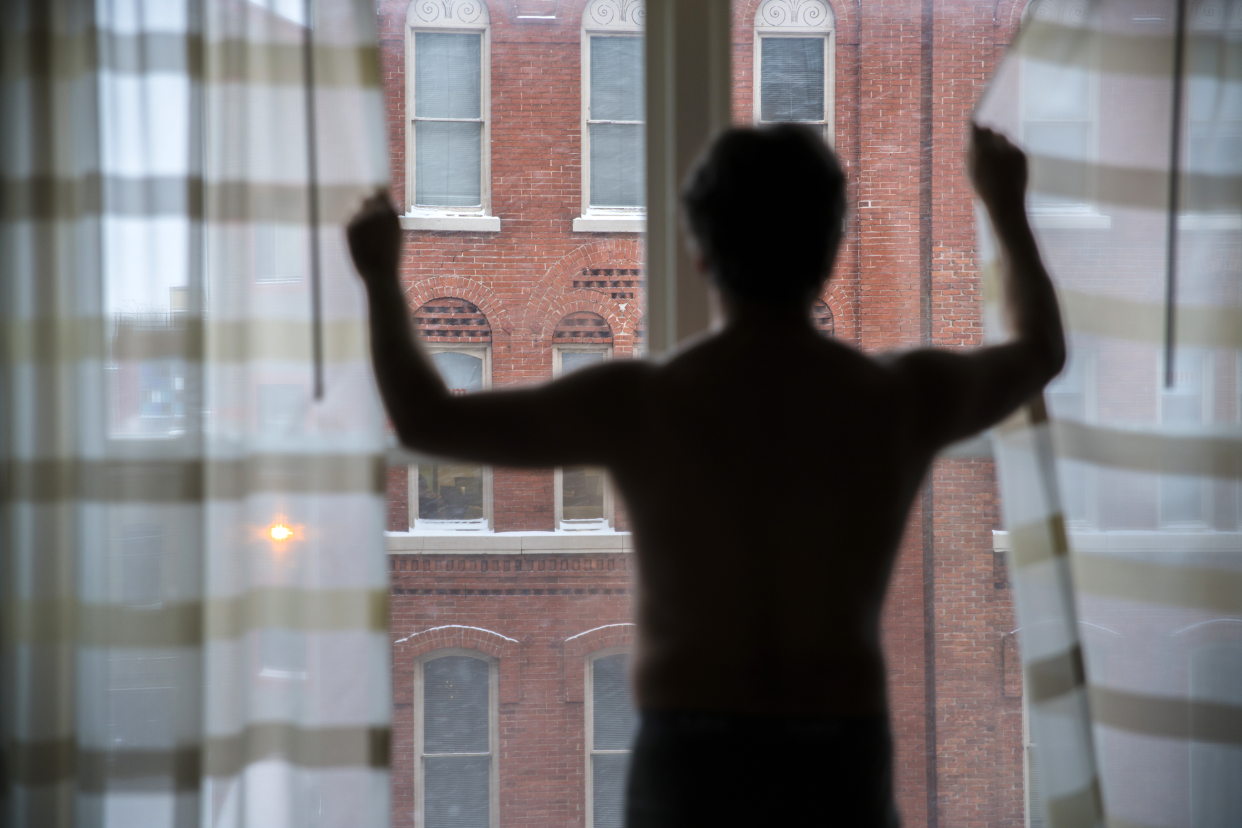 Naked man staring out of his apartment window