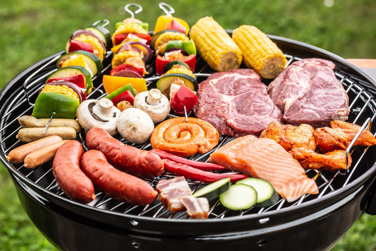 Broad assortment of raw bbq food placed on a grill ready to be barbecued on charcoal outdoors. One of our best grill picks. 