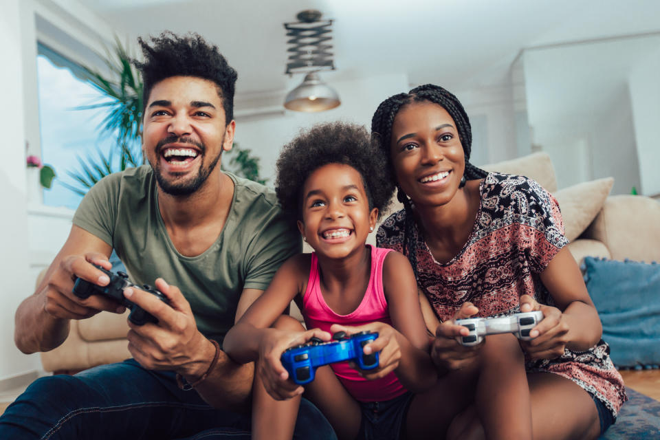 A man, woman, and child with video game controllers in their hand, sitting on a couch and smiling.