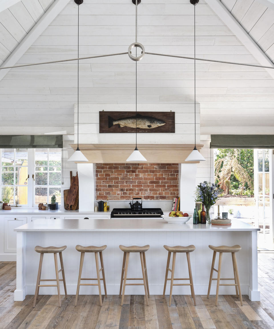 White kitchen with cladding and vaulted ceiling and island with bar stools in Cornish coastal newbuild