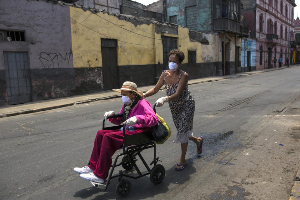 In this March 18, 2020 photo, Flor Vaso pushes her 84-year-old mother Carmen Reyes in a wheelchair to their home, in Lima, Peru. Vaso and her mother reside with 44 other families in a large, deteriorated house near the presidential palace that has earned it the nickname “Luriganchito,” or “Little Lurigancho,” after San Pedro de Lurigancho, the country’s most populous prison. (AP Photo/Rodrigo Abd)