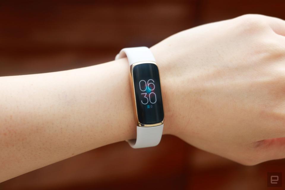 <p>Front view of the Fitbit Luxe with a light pink silicone band on a wrist against a dark brown background. The screen shows the time is 6:30pm.</p>
