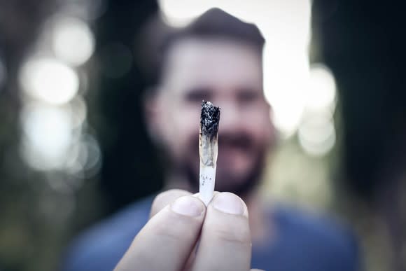 A man holding a lit cannabis joint in front of his face.