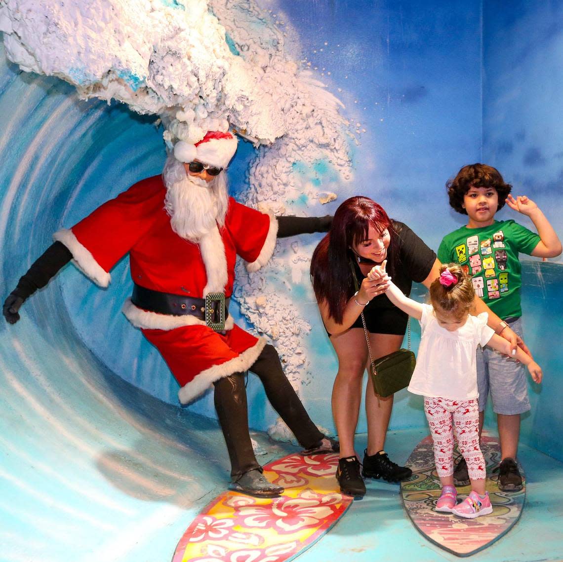 A family poses with surfing Santa Claus inside the newly reopened Santa’s Enchanted Forest at its new location within Hialeah Park in Hialeah, Florida, on Thursday, November 4, 2021.