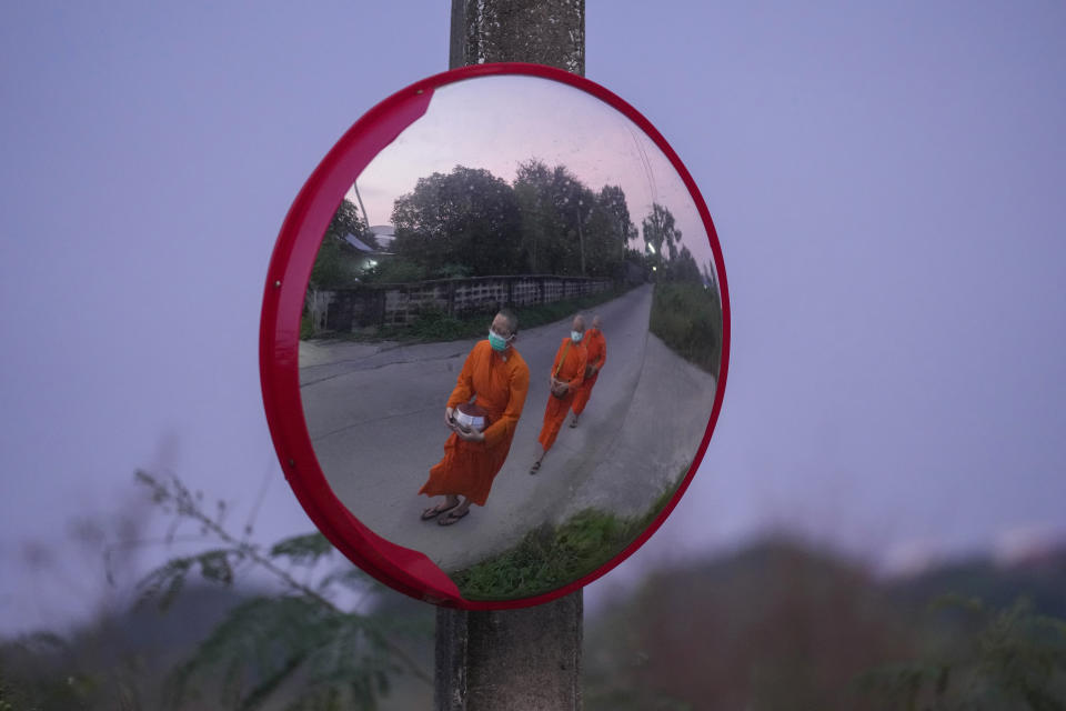 From left, Bhikkhuni Dhammavanna, Bhikkhuni Dhammaparipunna and Bhikkhuni Dhammasumana, are reflected in a mirror as they walk to collect alms from devotees in Nakhon Pathom province on Sunday, Nov. 21, 2021. Women are banned from becoming monks in Thailand, where over 90% of the population is Buddhist. Historically, women could only become white-cloaked nuns often treated as glorified temple housekeepers. But dozens have traveled to Sri Lanka to receive full ordination. (AP Photo/Sakchai Lalit)