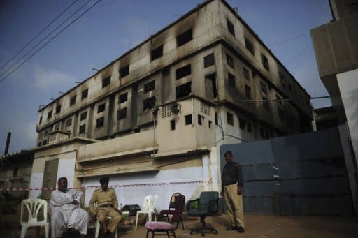 Pakistani security officials sit outside the burnt-out garment factory in Karachi. Three factory-owners facing murder charges over the deaths of 289 people in a huge fire in Karachi handed themselves in to court as Pakistan police described the moment the flames took hold