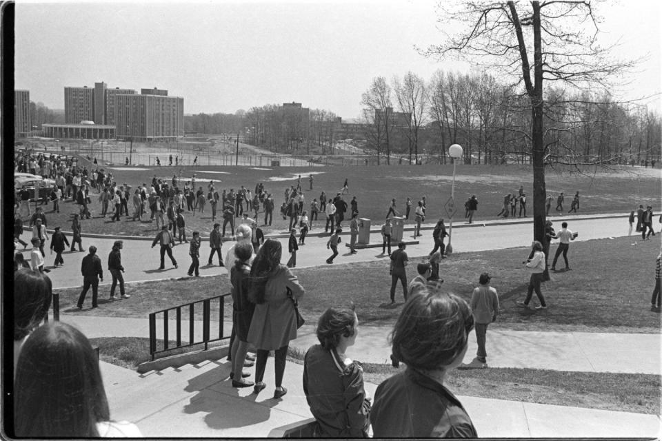 PUBLISHED CAPTION: Just before guardsmen begin firing, several students stop on the south balcony of Taylor Hall to watch the protests. Onlookers begin to react as gunfire erupts from the hill.
Photographers notes: Kent State University - May 4 , 1940- Photo by Paul Tople (COPYRIGHT ALL RIGHTS RESERVERED). Photographs taken from the south balcony of Taylor Hall just before, during and after the National Guard opened fire on the students. Seconds before the National Guard moves to the top of the hill by the pagoda and turns to fire.. students watch activities. Photo taken looking to the south east with the practice field center right. One of the victims, Jeff Miller wearing a cowboy shirt center walks towards the road where he is fatally shot.