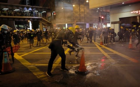 A protester uses a traffic cone to cover a tear gas canister - Credit: AP