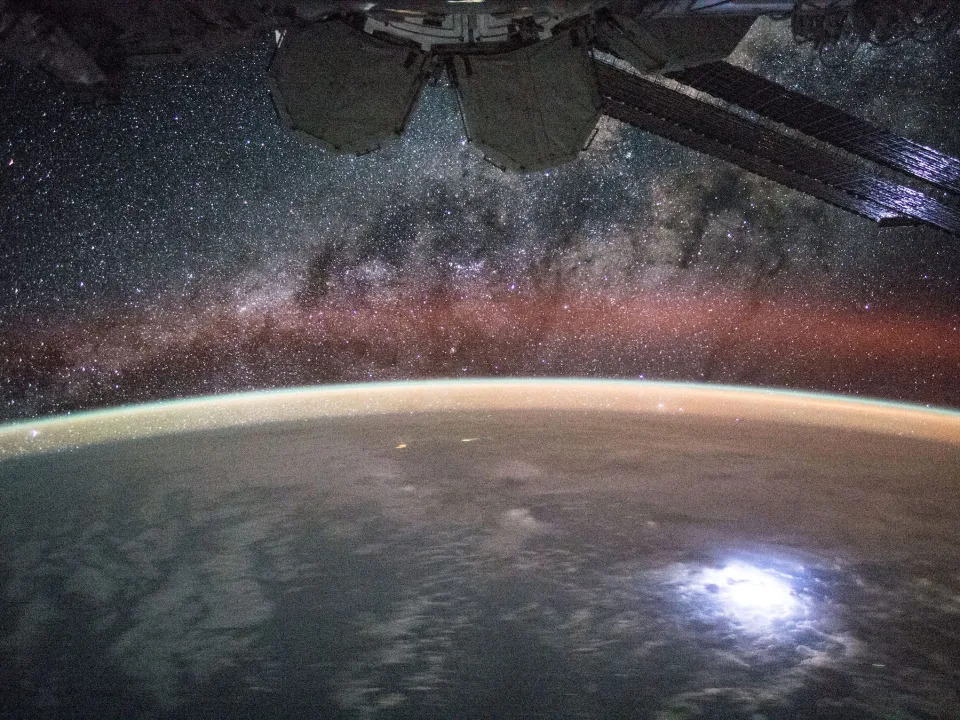 earth with bright spot lightning strike with starry milky way purple and black above and solar panels of space station in foreground