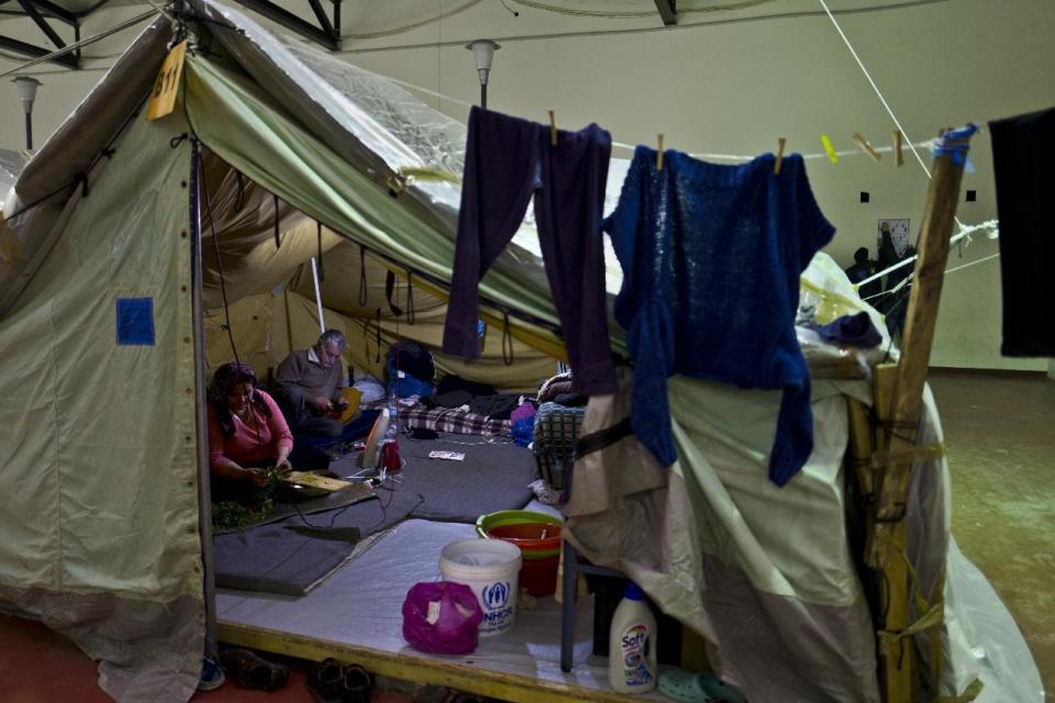 In this Tuesday, Jan. 17, 2017 photo, a Syrian refugee woman cuts vegetables while her husband checks his mobile phone at their tent in Kalochori refugee camp on the outskirts of the northern Greek city of Thessaloniki. (AP Photo/Muhammed Muheisen)