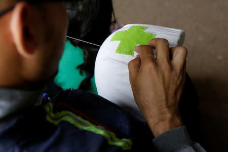 A volunteer sews a green cross to his helmet while he waits for the planning of the day to help injured demonstrators in Caracas, Venezuela April 22, 2017. REUTERS/Marco Bello