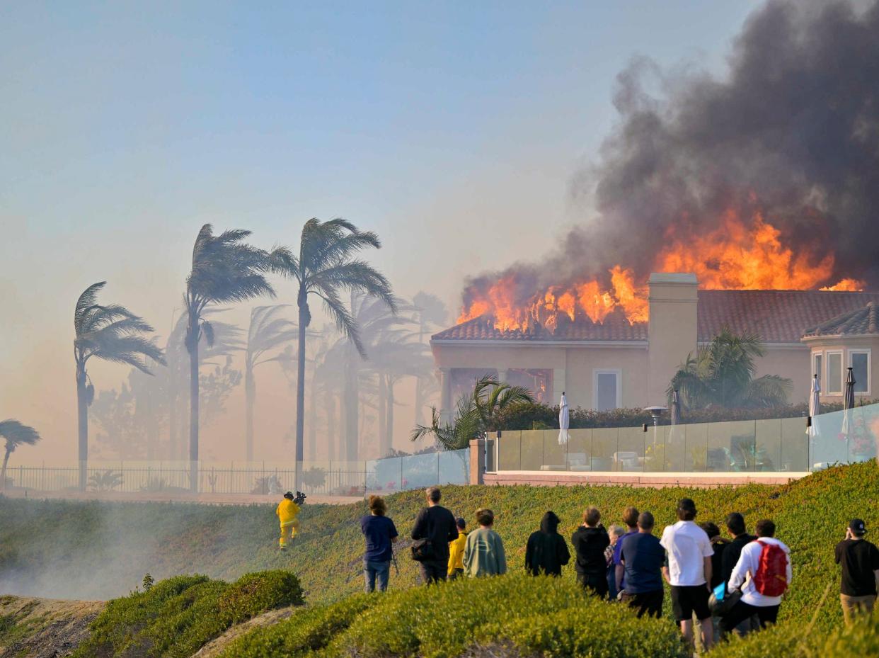 group of people watch wildfire burning home in the hills with palm trees