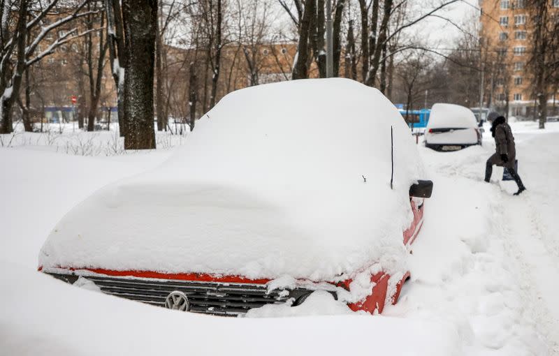 A pedestrian walks near cars covered with snow in a street in Moscow