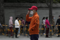 A volunteer wearing a red cap adjusts his mask as residents line up for mass COVID test, Wednesday, April 27, 2022, in Beijing. Workers put up fencing and police restricted who could leave a locked-down area in Beijing on Tuesday as authorities in the Chinese capital stepped up efforts to prevent a major COVID-19 outbreak like the one that has all but shut down the city of Shanghai. (AP Photo/Ng Han Guan)