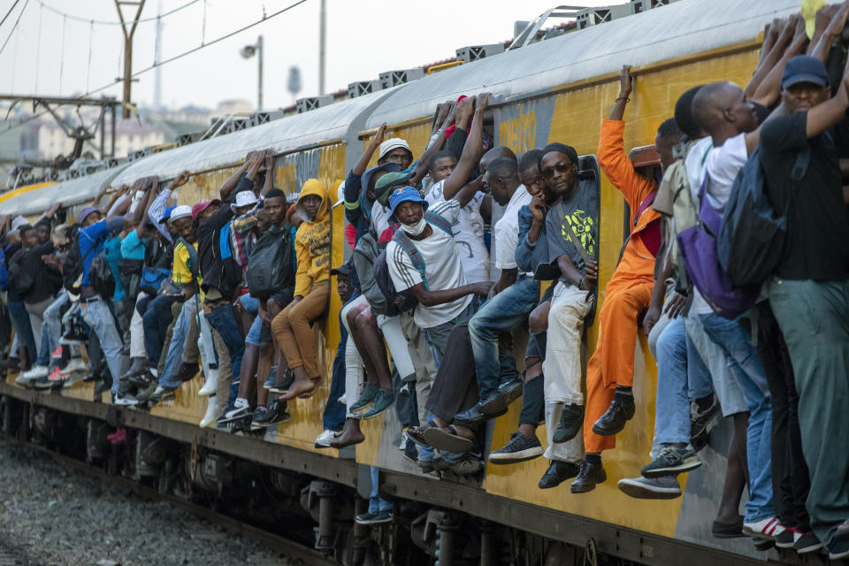 FILE - Train commuters hold on to the side of an overcrowded passenger train in Soweto, South Africa. Monday, March 16, 2020. South Africans celebrate "Freedom Day" every April 27, when they remember their country's pivotal first democratic elections in 1994 that announced the official end of the racial segregation and oppression of apartheid.(AP Photo/Themba Hadebe, File)