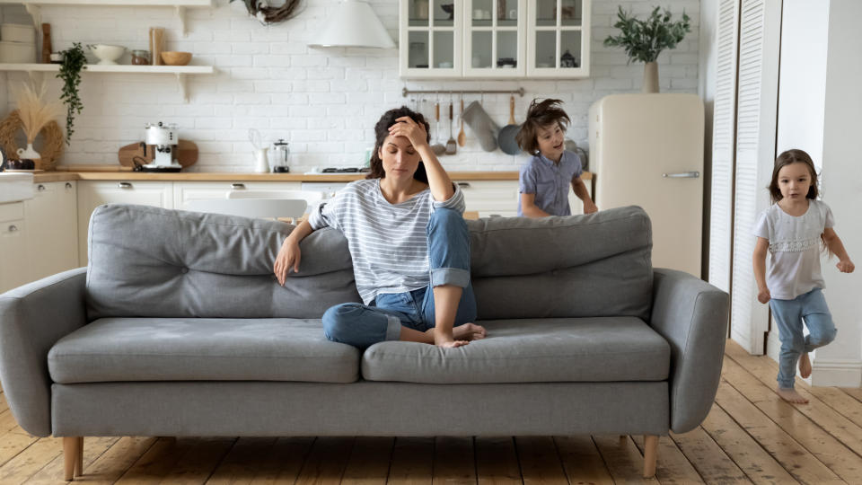 Mother sits on couch as children run around